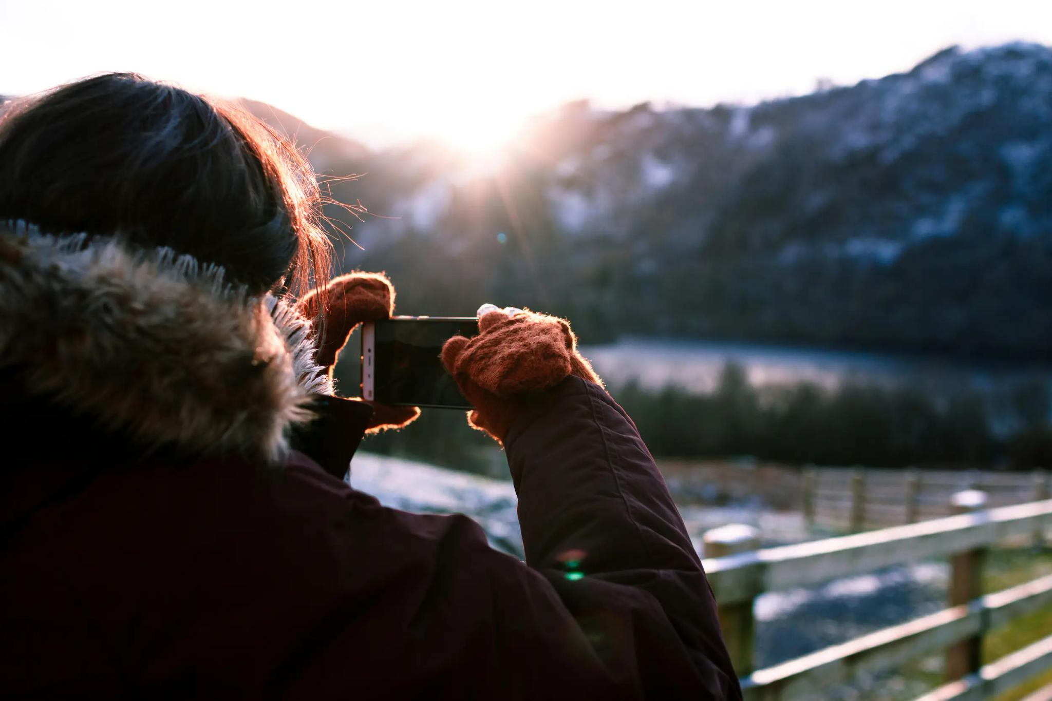 Person fotografiert Sonnenuntergang in winterlicher Landschaft.