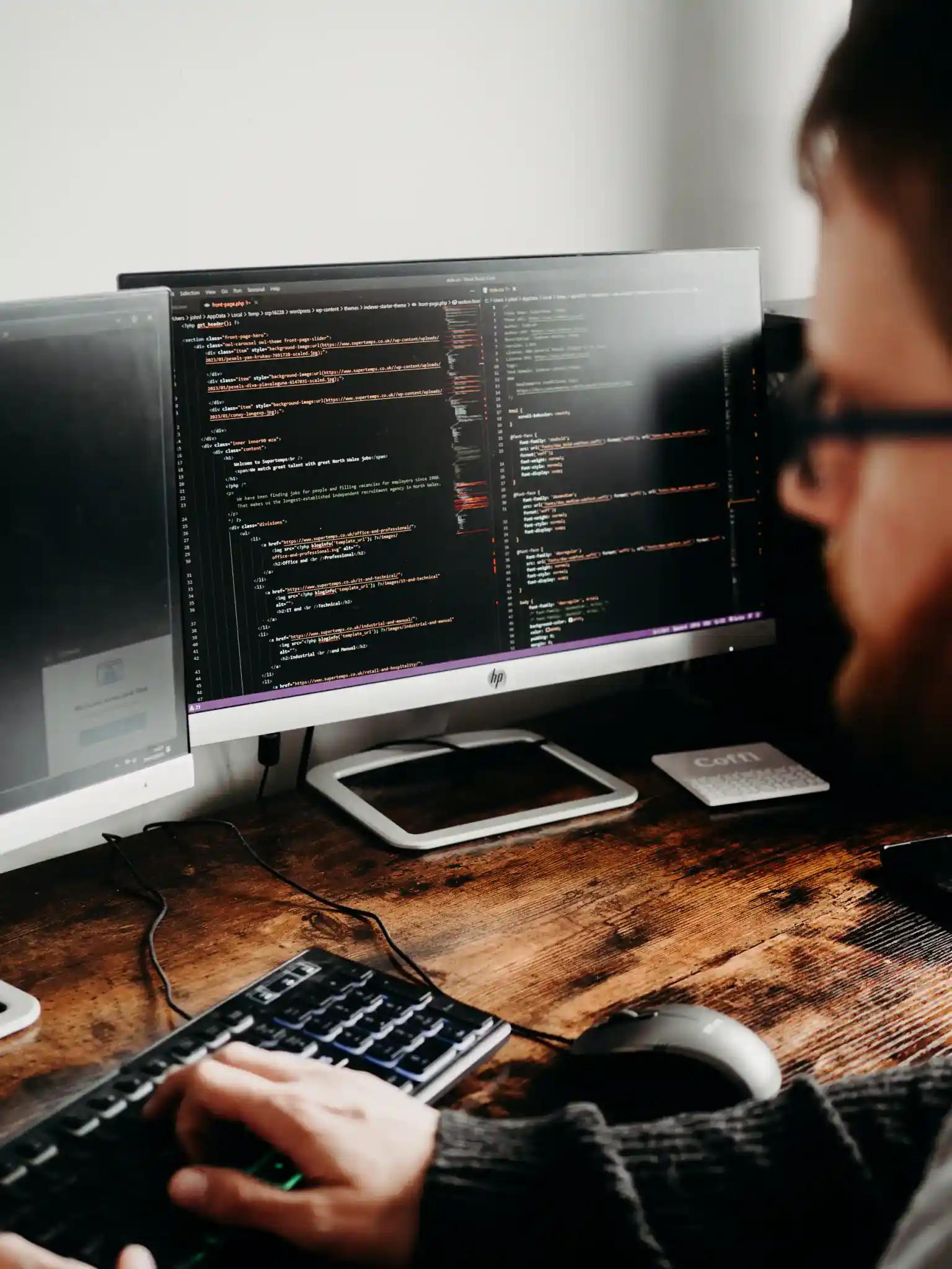 Person, der am Computer mit mehreren Monitoren programmiert.