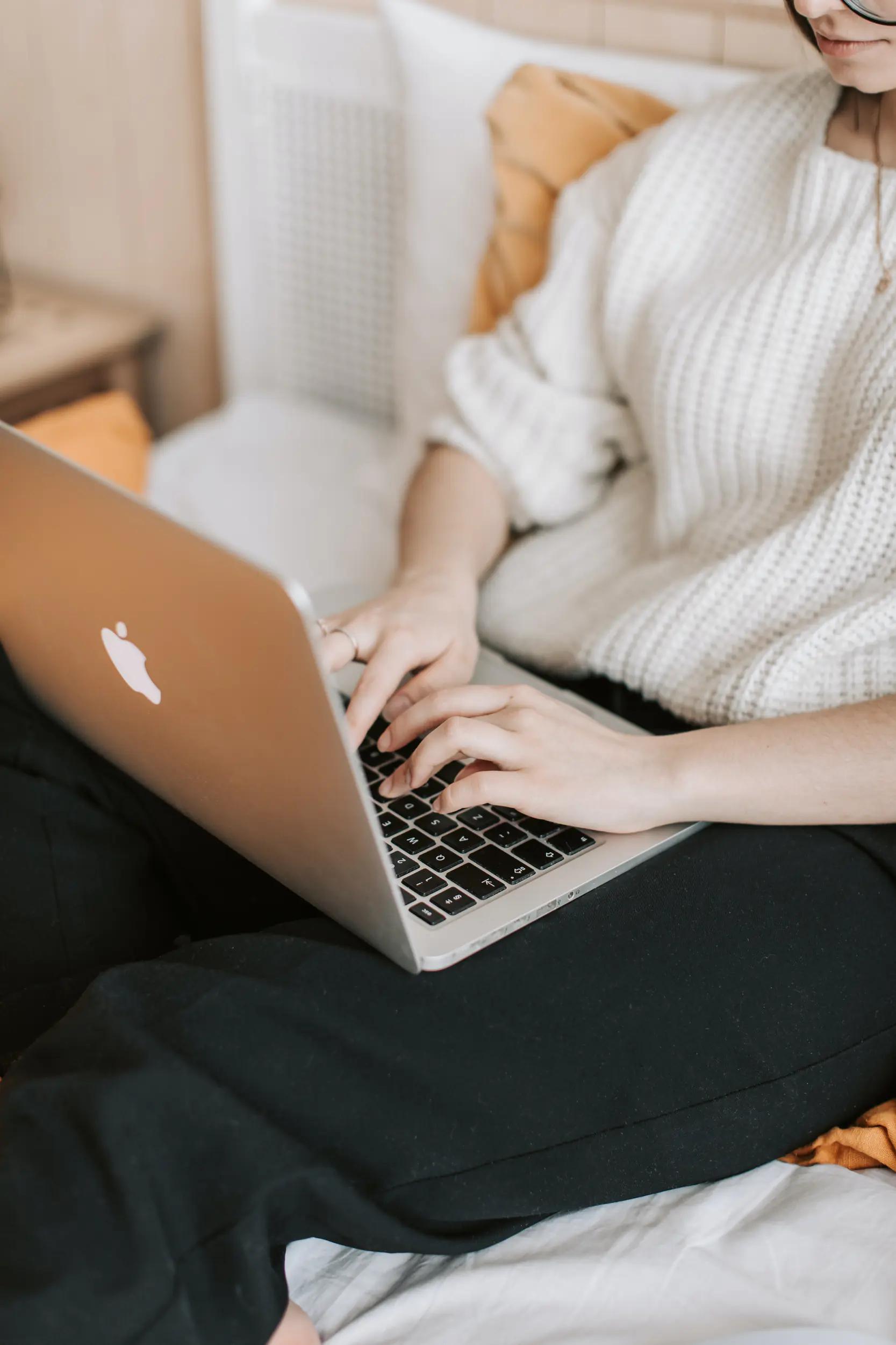 Frau arbeitet an Laptop sitzend auf Sofa.