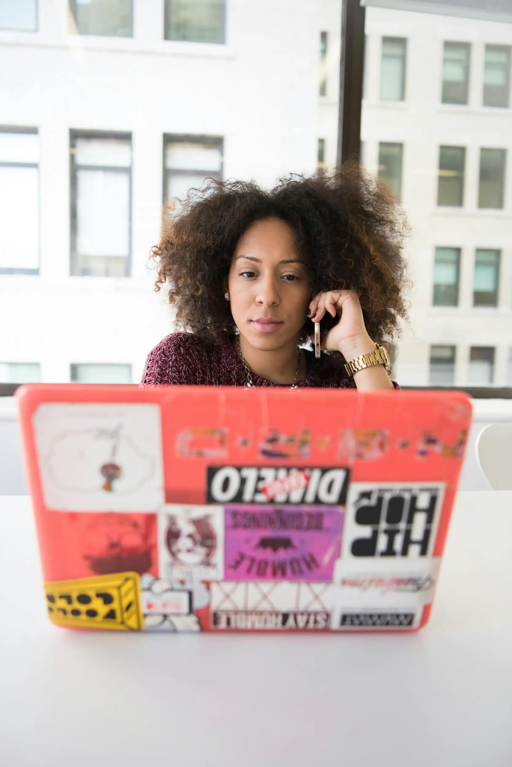Woman with curly hair working on a laptop and talking on the phone.