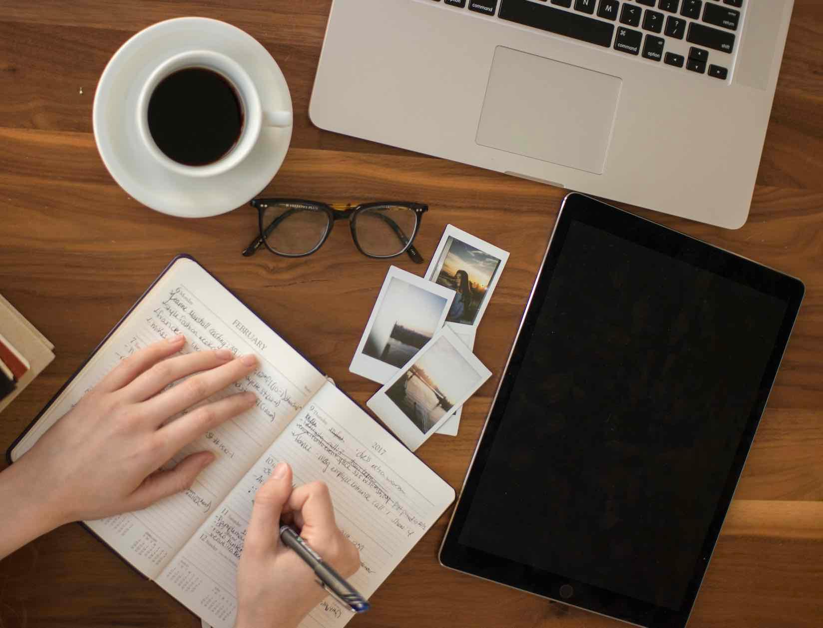 Workspace with notebook, tablet, laptop, coffee, and photos.