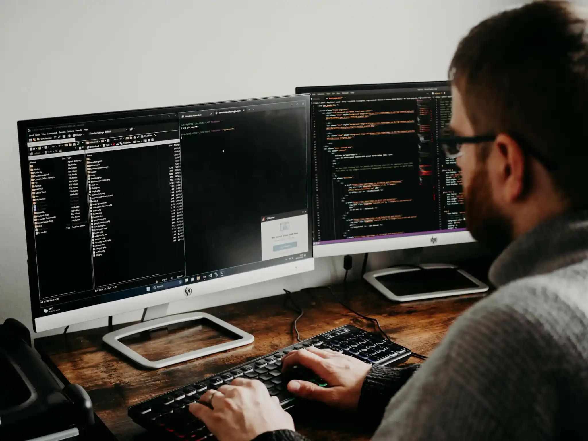 Person arbeitet an zwei Monitoren mit Code
