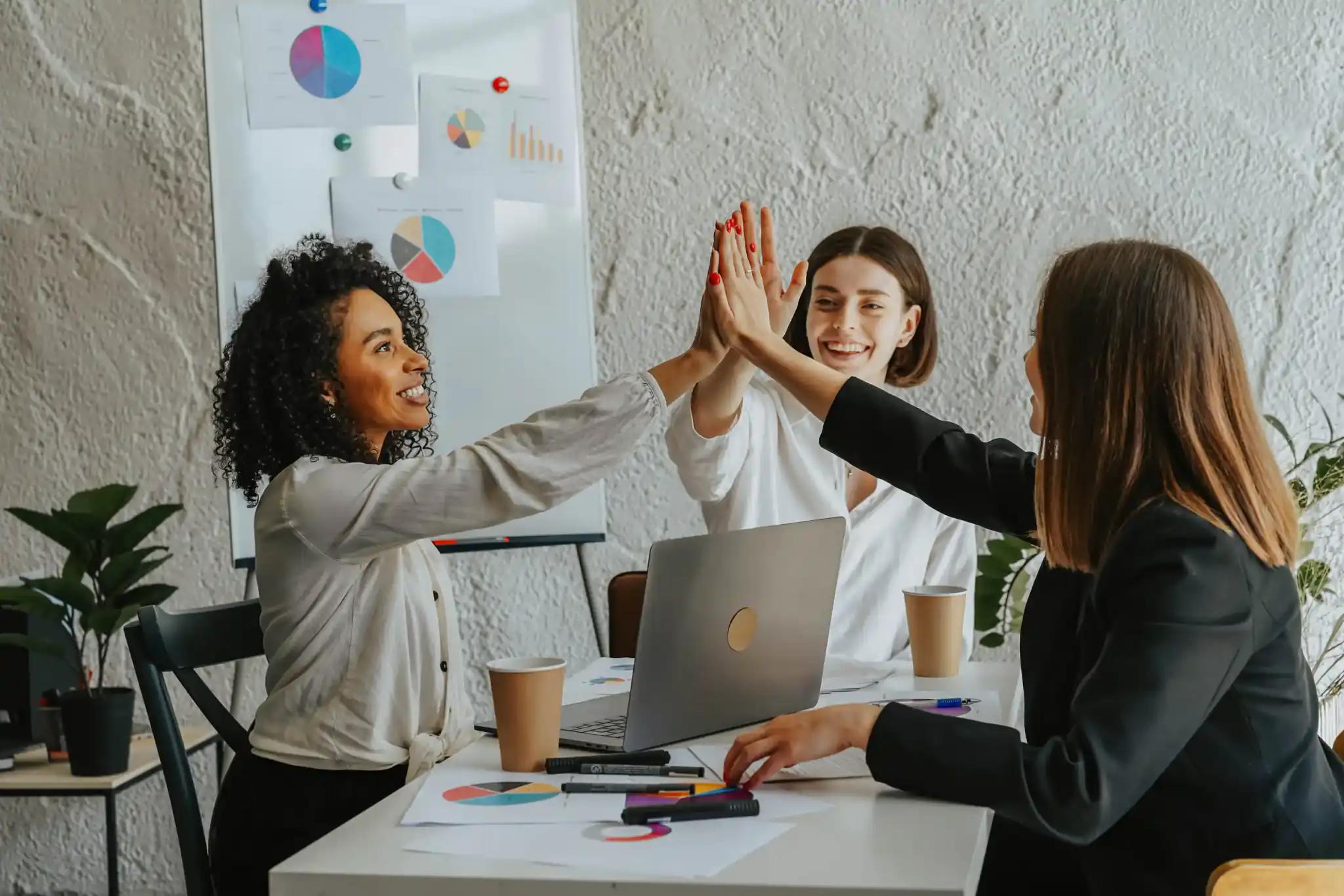 Drei Frauen geben sich am Konferenztisch High Five.