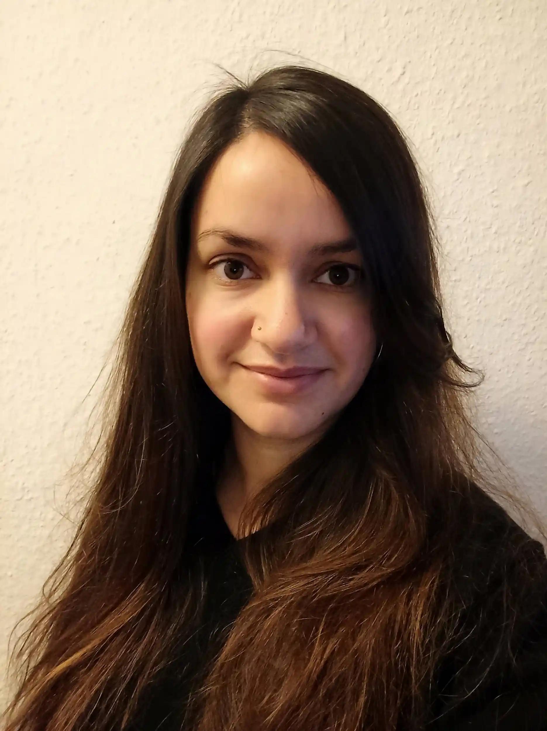 Portrait of a woman with long dark hair against a light wall.