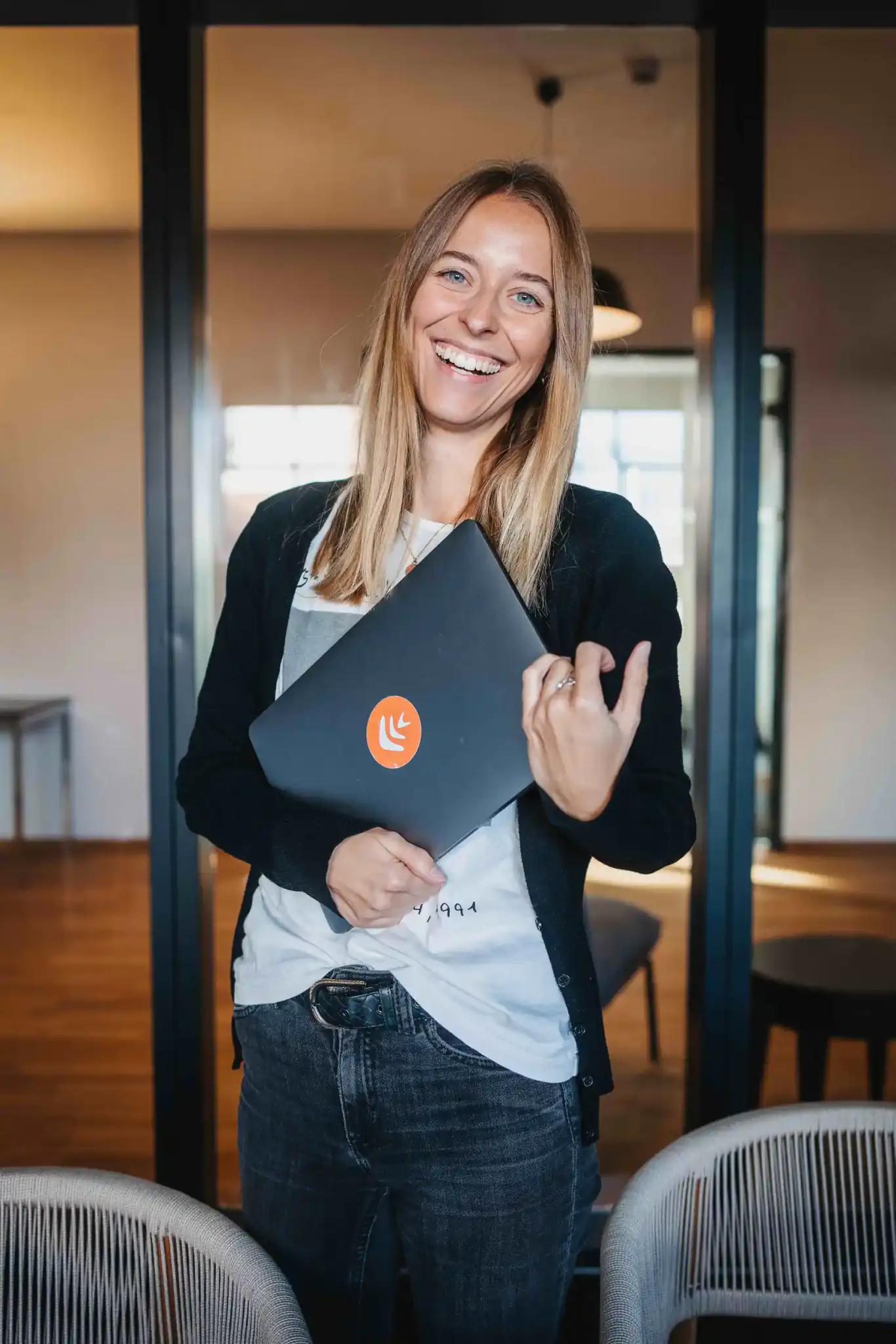 Frau mit Laptop lächelt in einem Büro.
