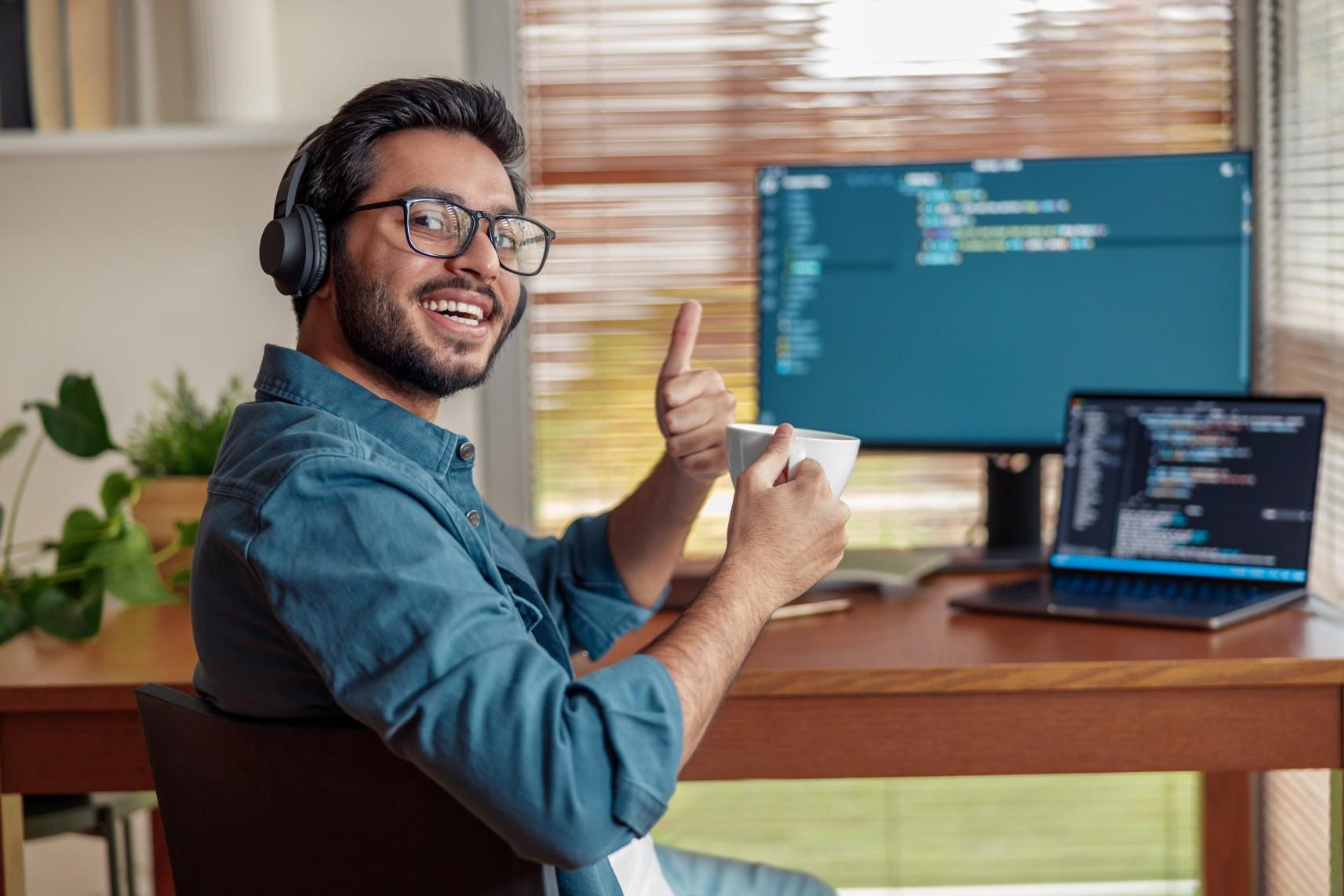 Mann mit Kopfhörern, der am Computer programmiert und Daumen hoch zeigt.