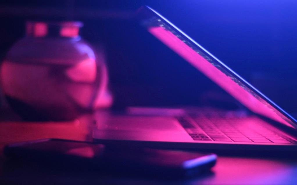 Halbgeöffnetes Laptop und Smartphone auf Tisch mit rosa-blauem Licht
