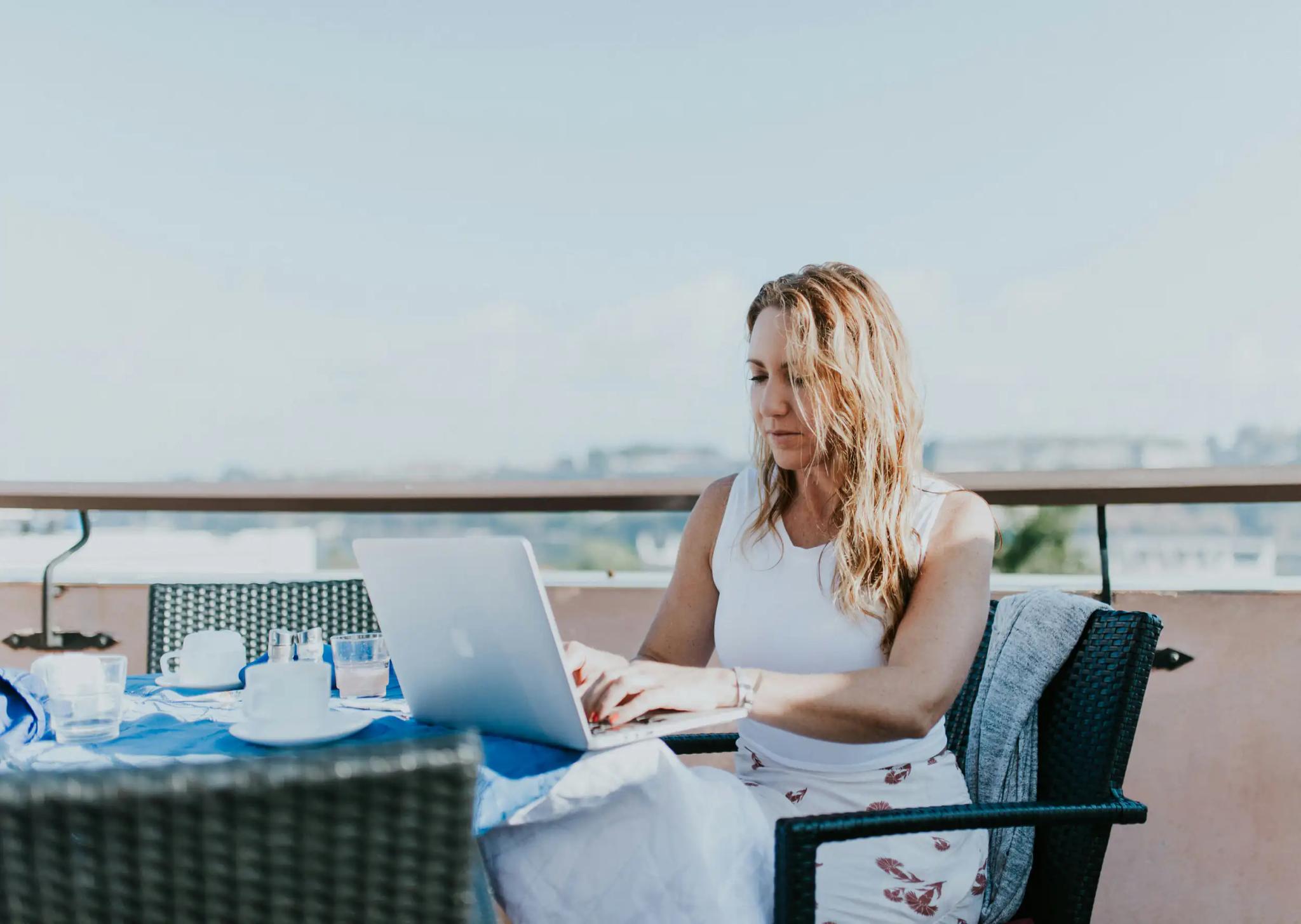 Woman working on laptop outdoors on a terrace.