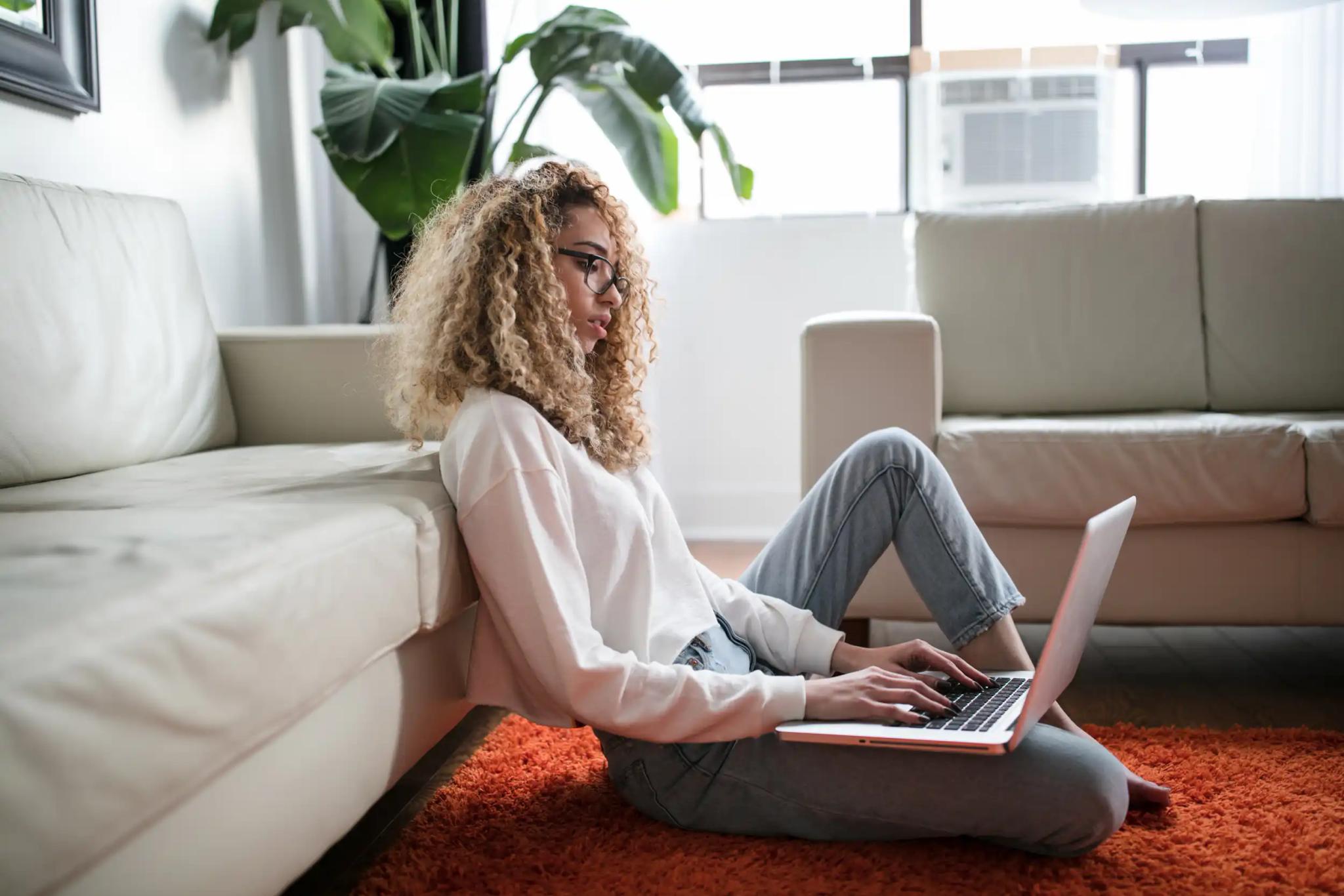 Woman sitting on the floor in front of her couch working on the laptop.