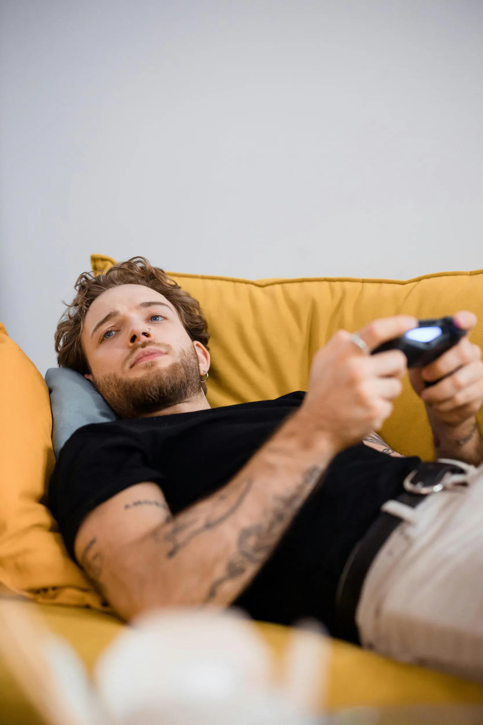 Man lying on yellow couch playing video game.