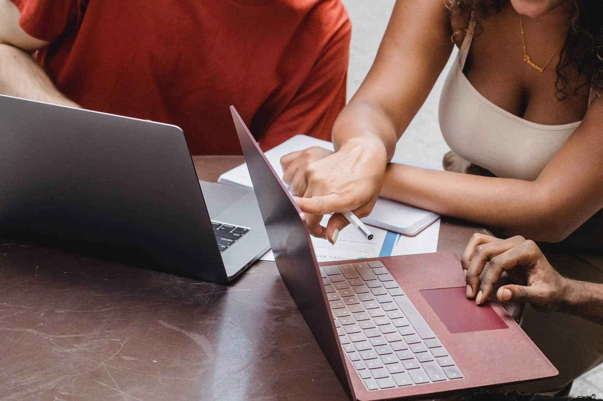 Menschen arbeiten gemeinsam an Laptops am Tisch.