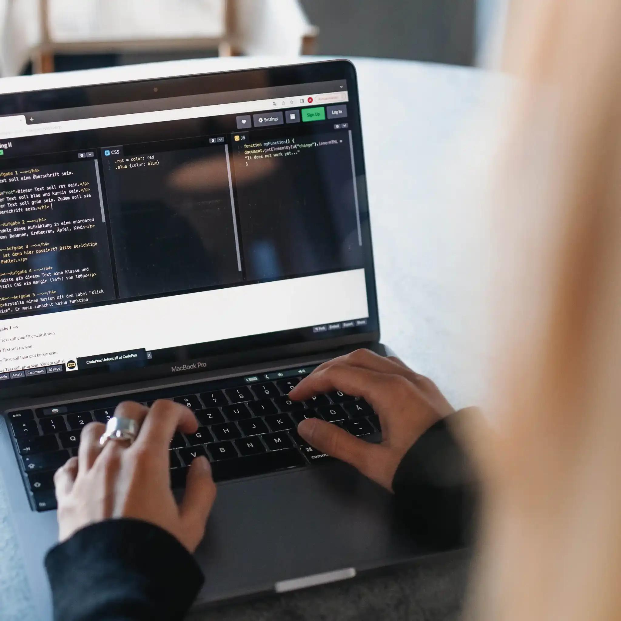 Person typing on a laptop with programming code on the screen.