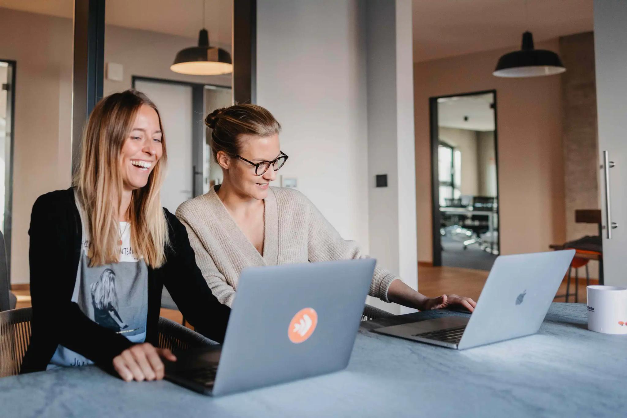 Two women working together on laptops.