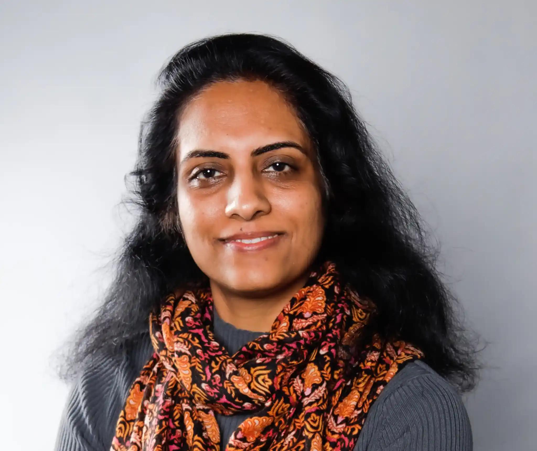 Smiling woman with scarf against neutral background.