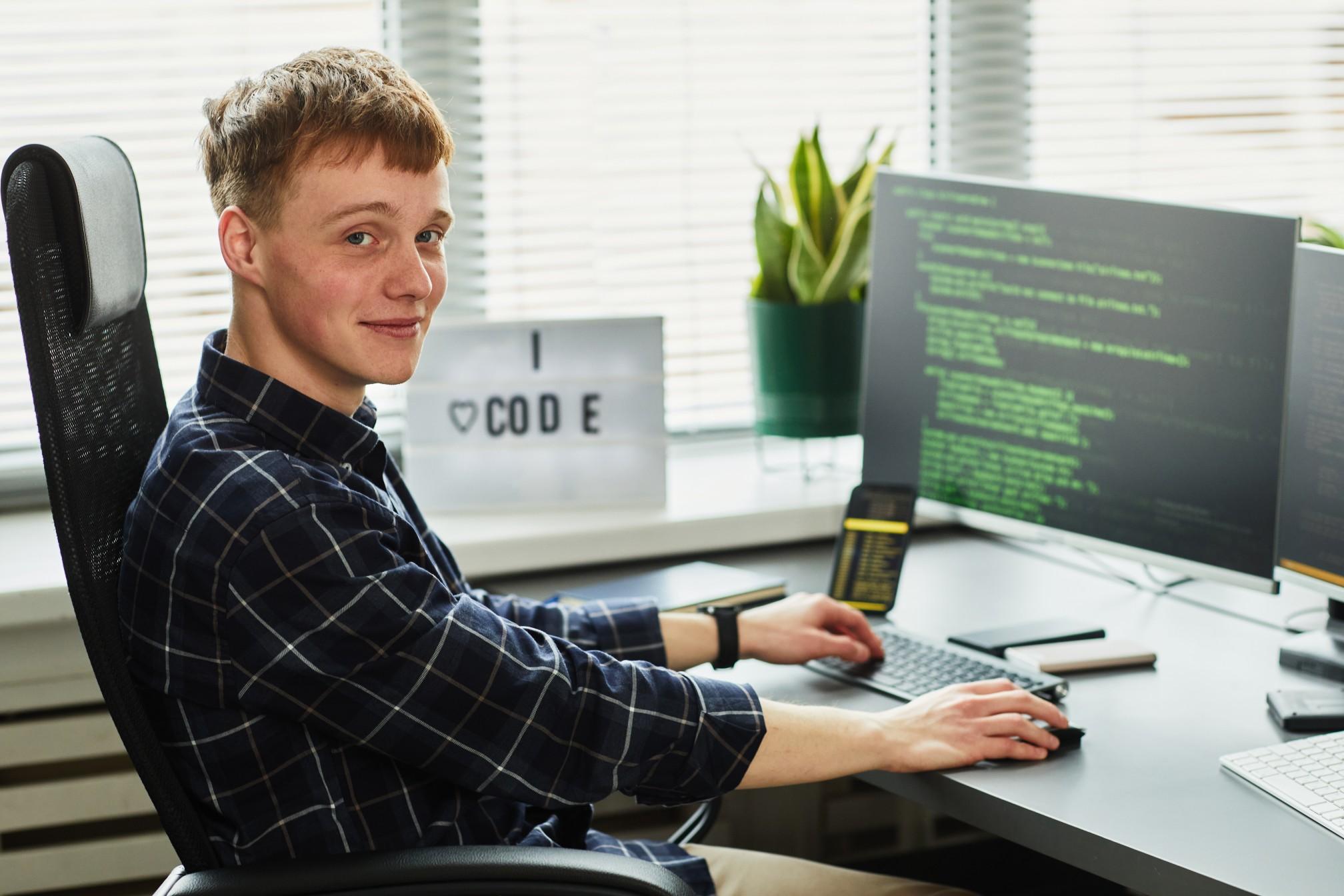 Young man sitting at desk coding on computer.