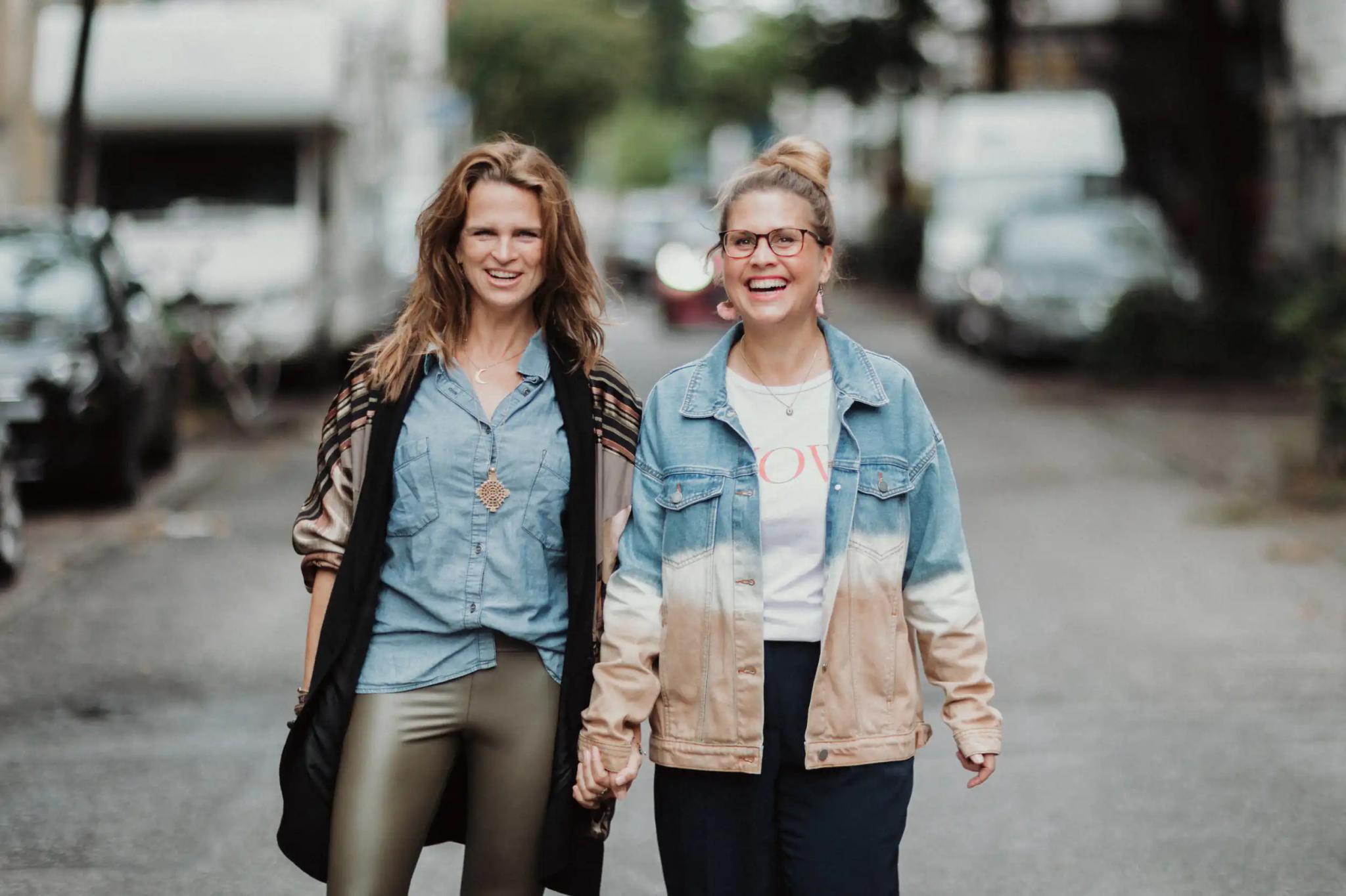 Two women holding hands walking on a street.