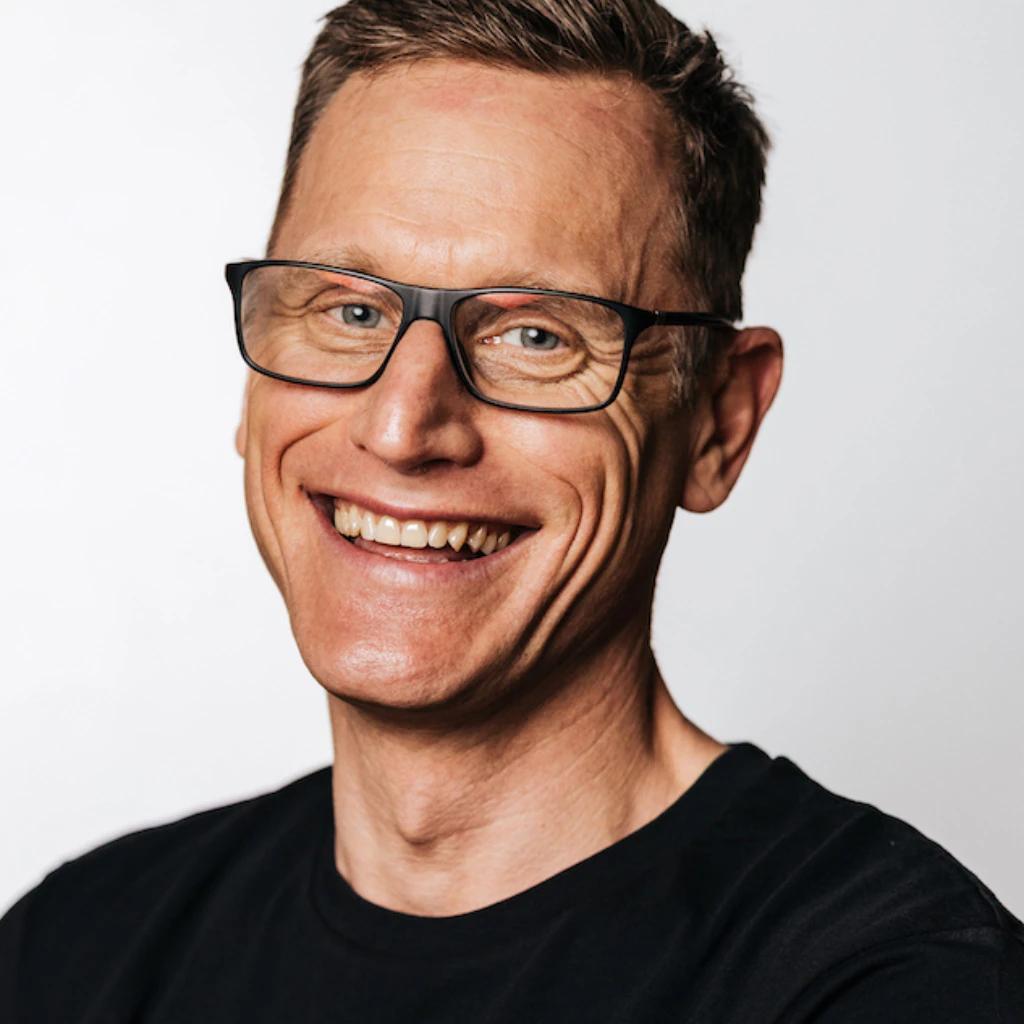 Porträt eines lächelnden Mannes mit Brille.