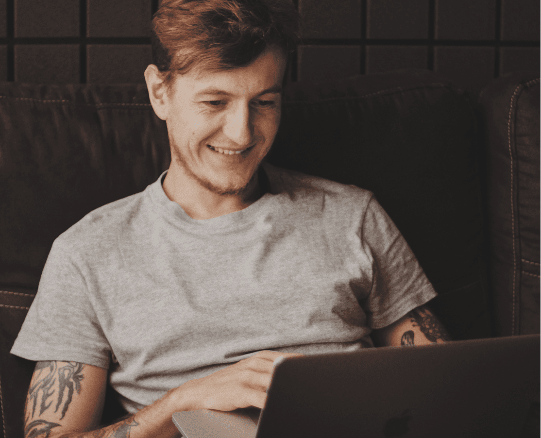 Lächelnder Mann mit Tattoo nutzt Laptop auf der Couch
