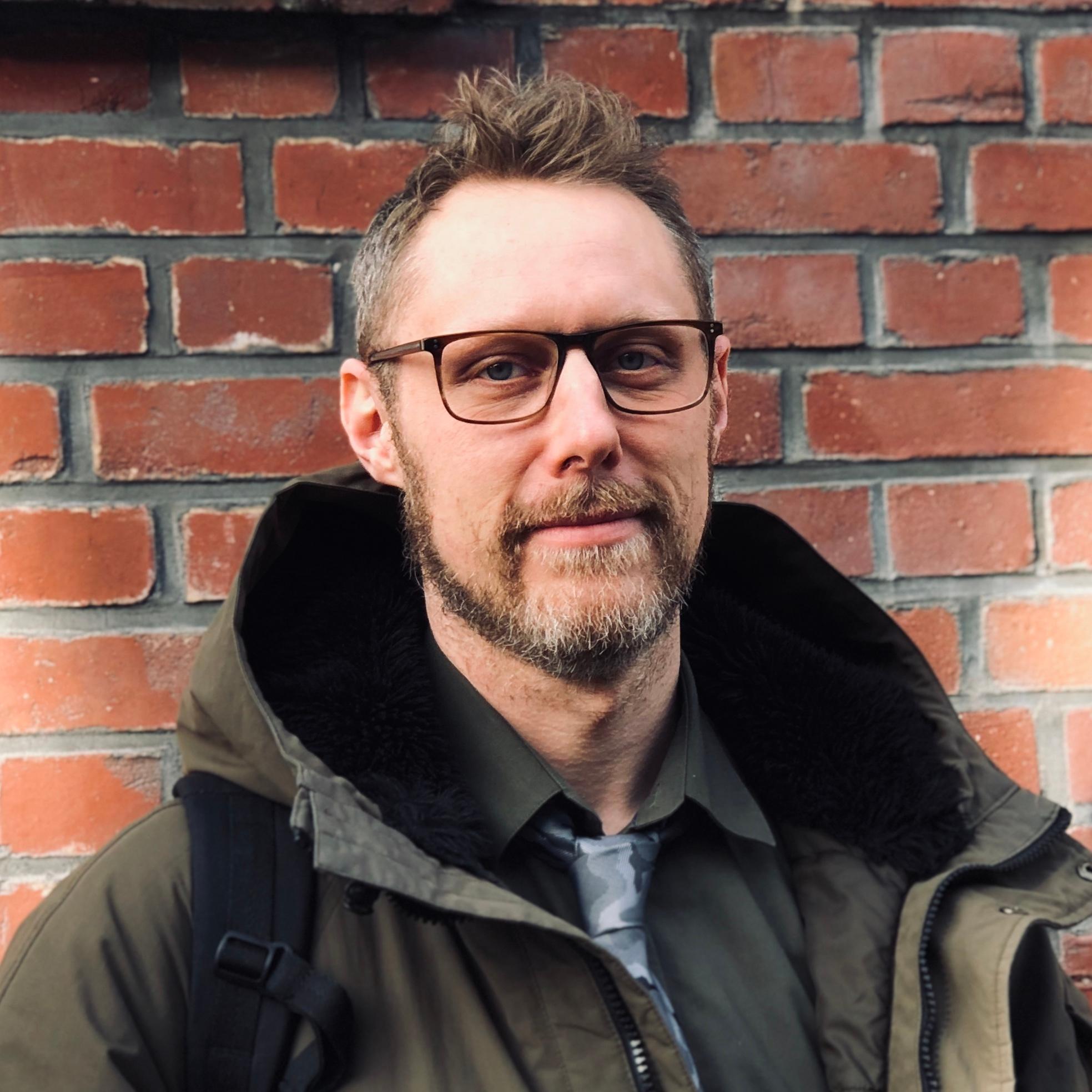 Portrait of a man wearing glasses in front of a brick wall