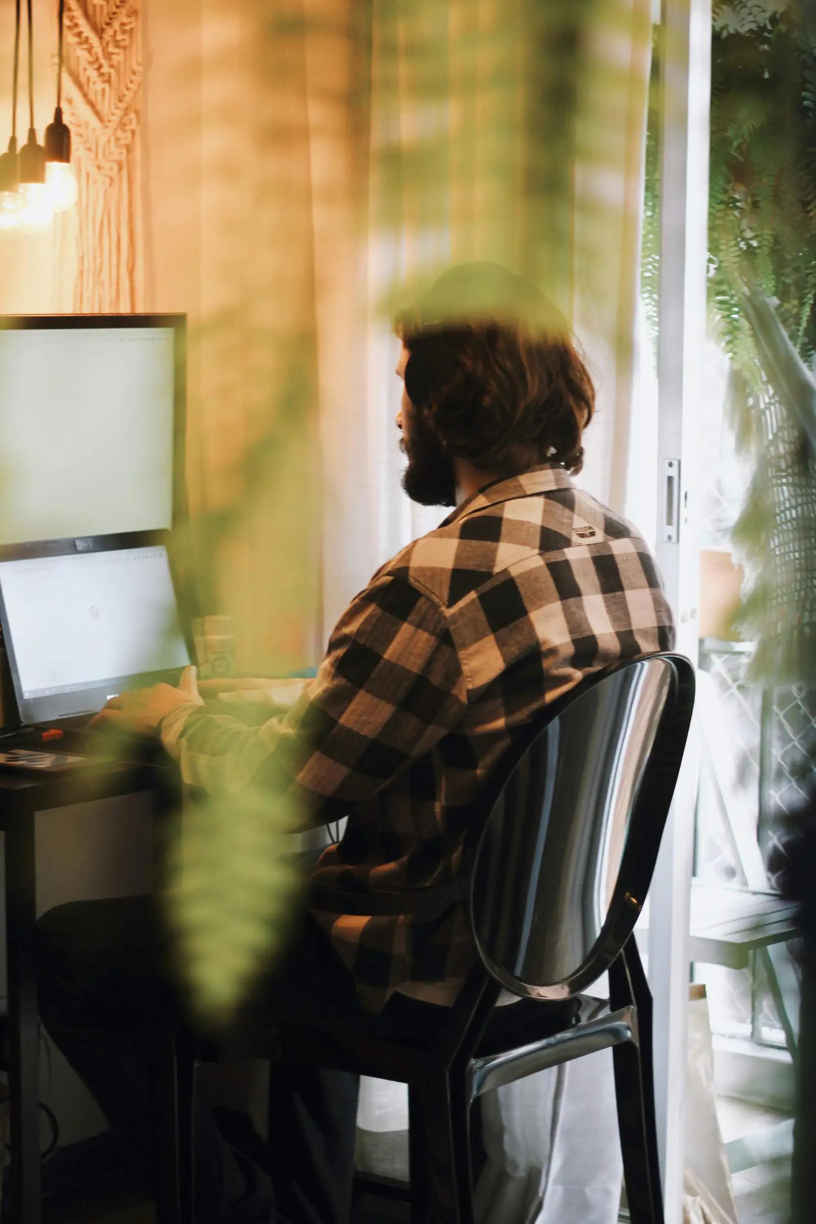 Mann sitzt am Schreibtisch und arbeitet am Computer, umgeben von Pflanzen.