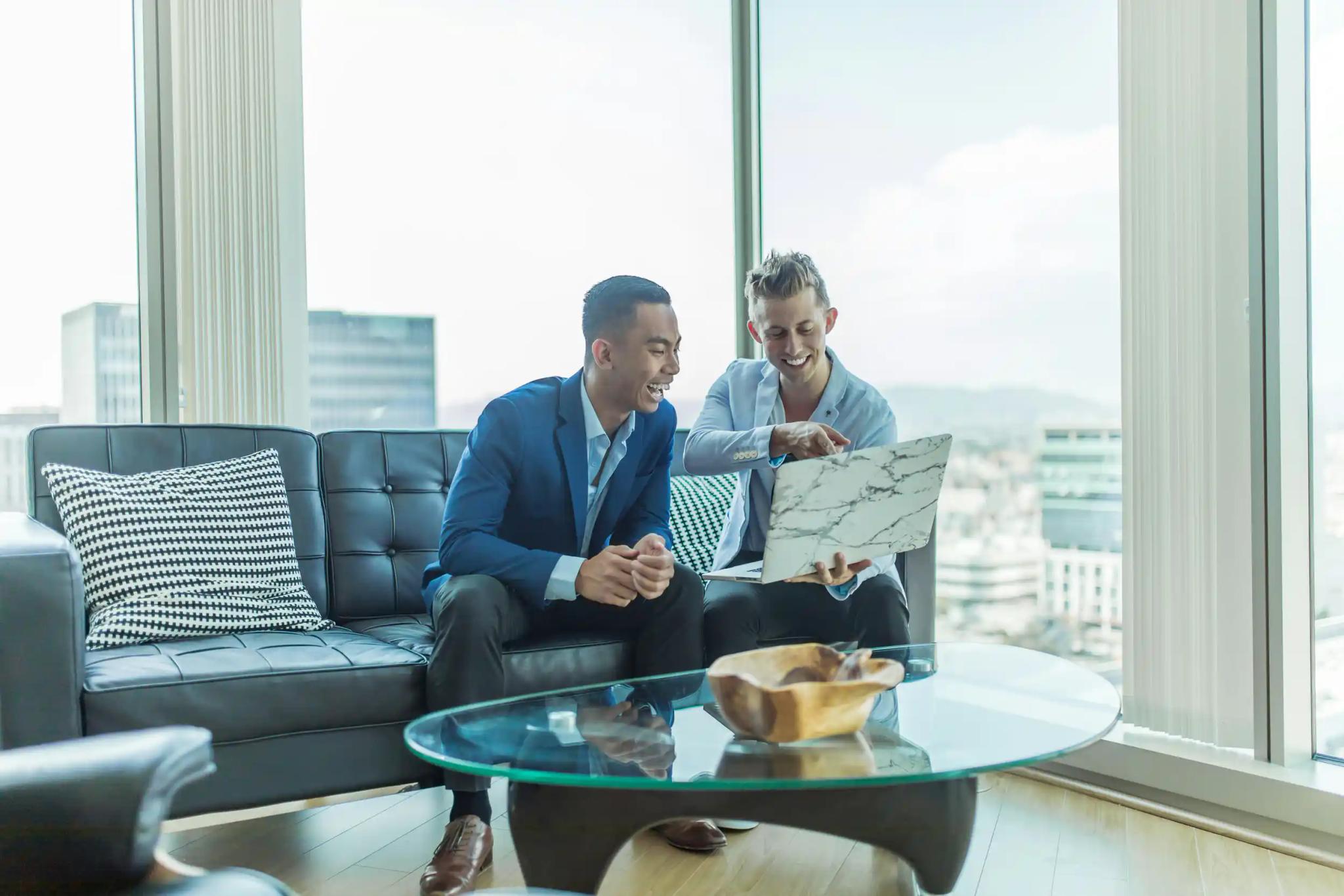 Two men sitting on a couch together with a laptop.