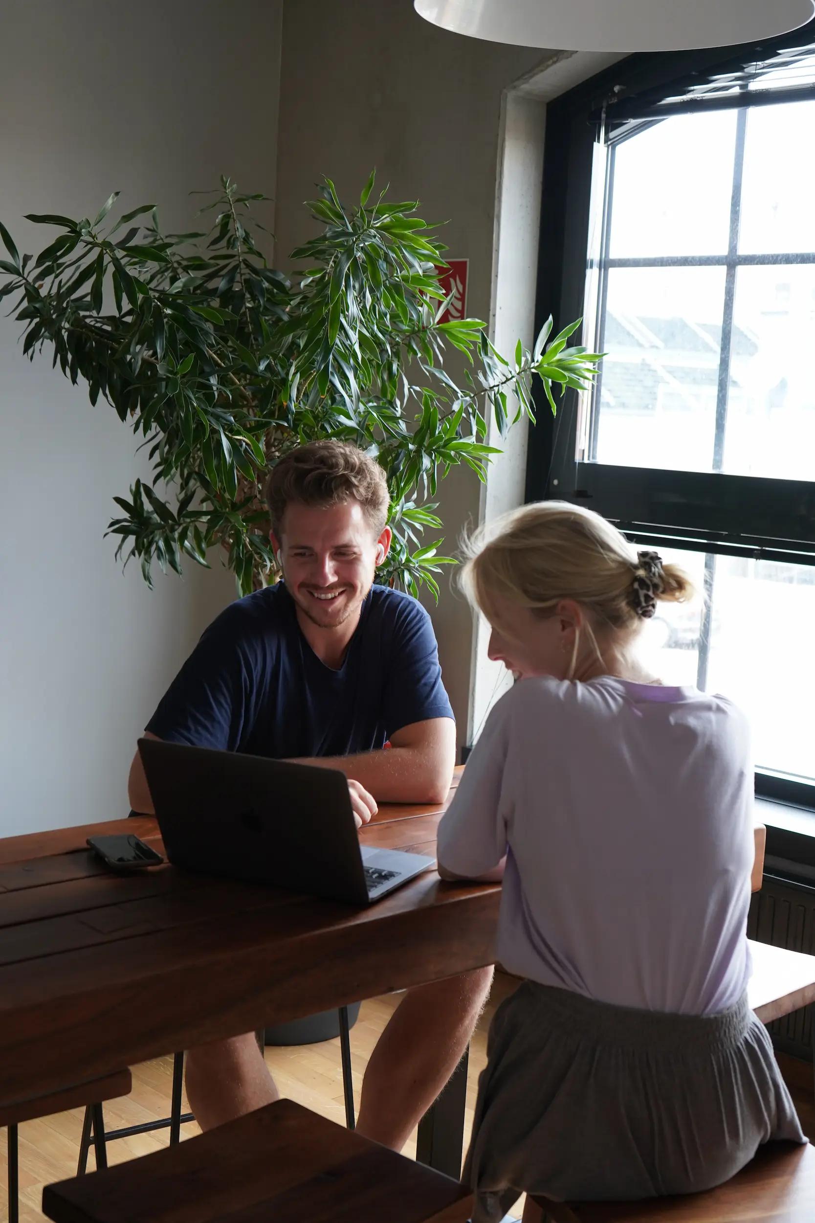 Two people working together on a laptop at a wooden table.
