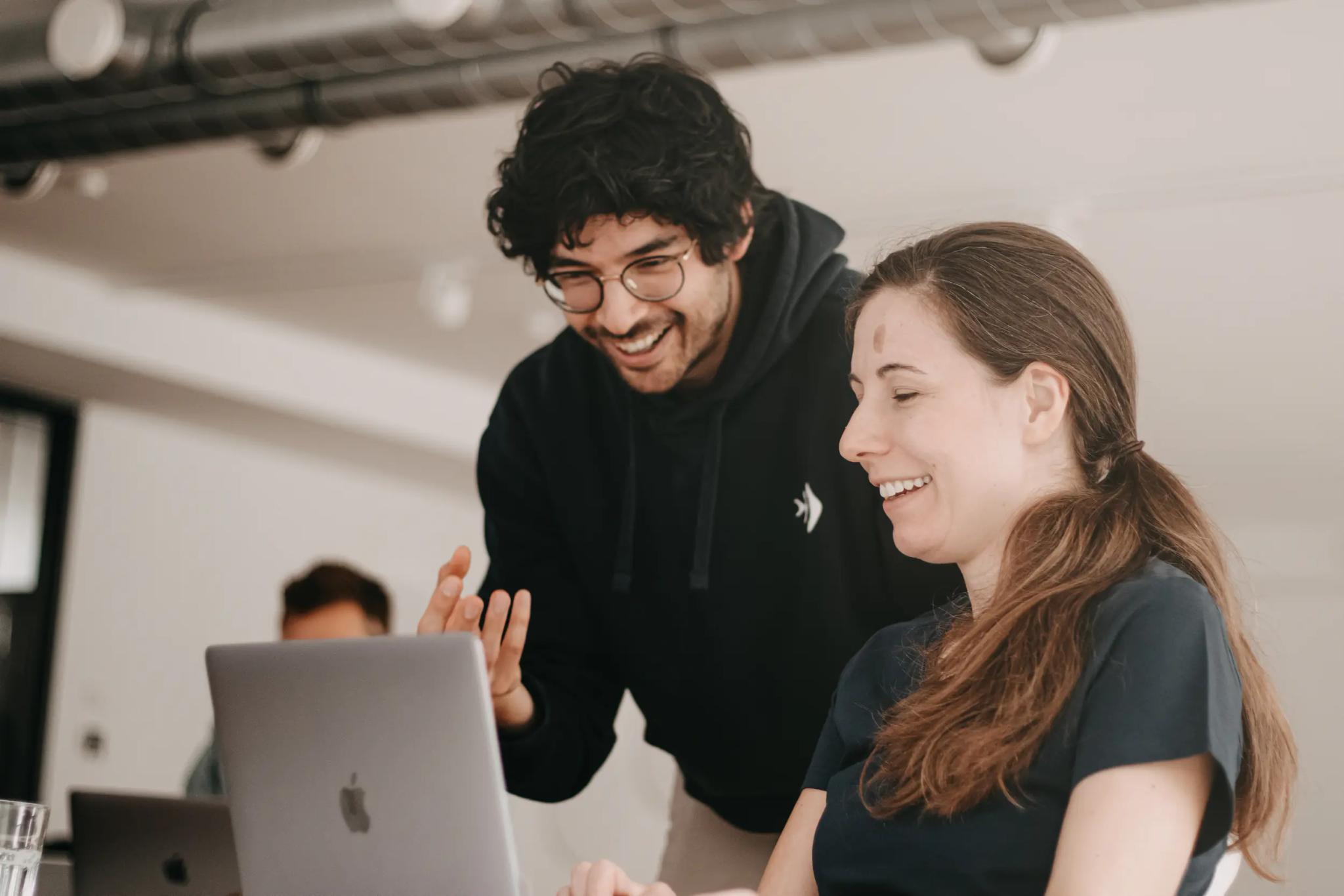 Zwei Personen, die zusammen an einem Laptop arbeiten und lachen.