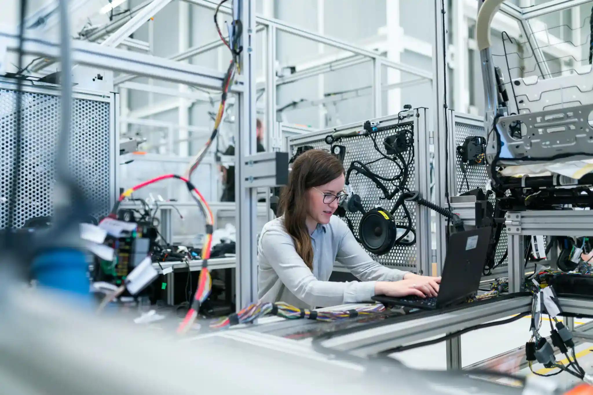 Frau arbeitet an Laptop in moderner Fabrikhalle.