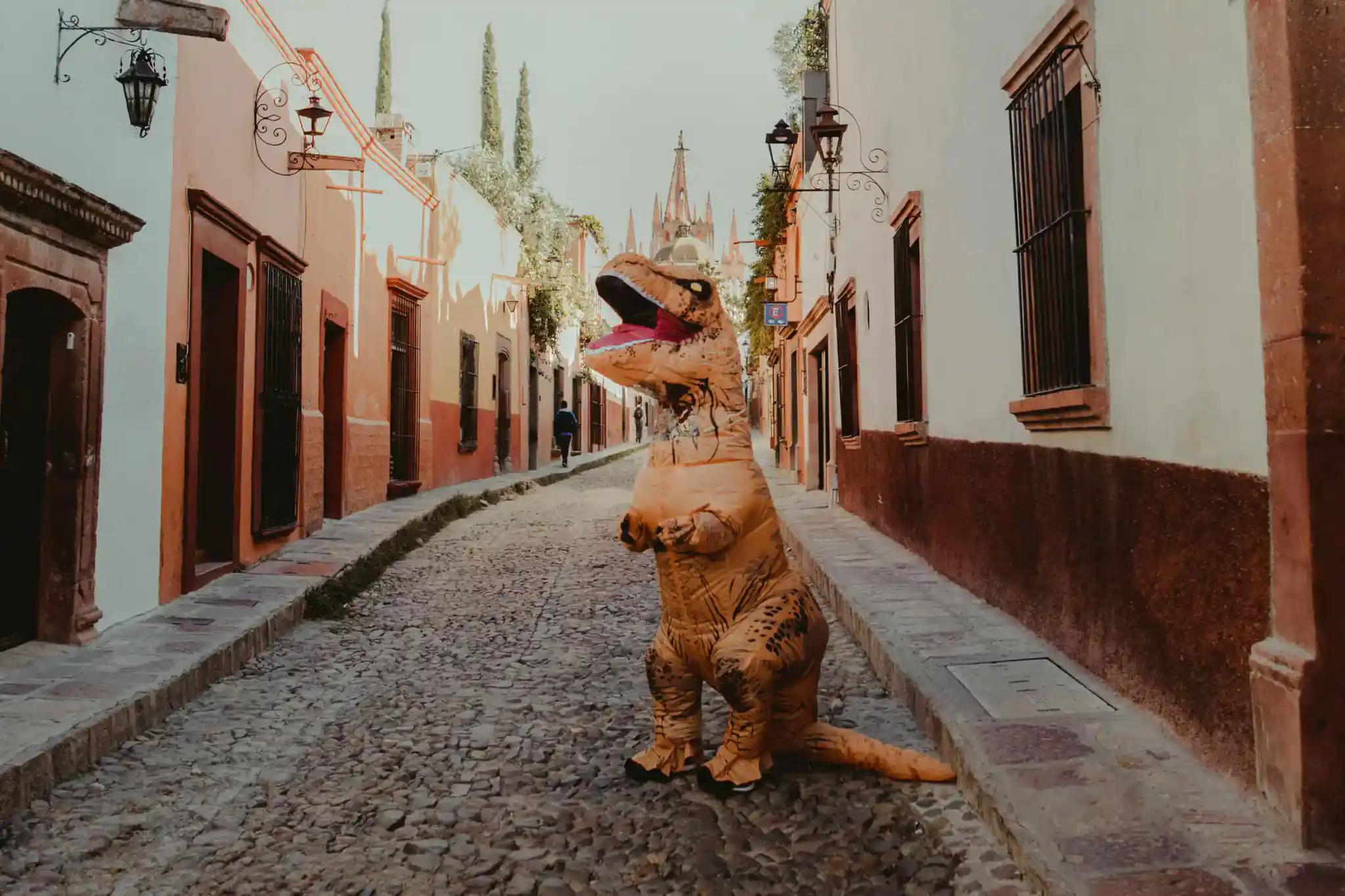 Person in Dinosaurier-Kostüm auf einer Straßenpflasterung in einer Stadt.