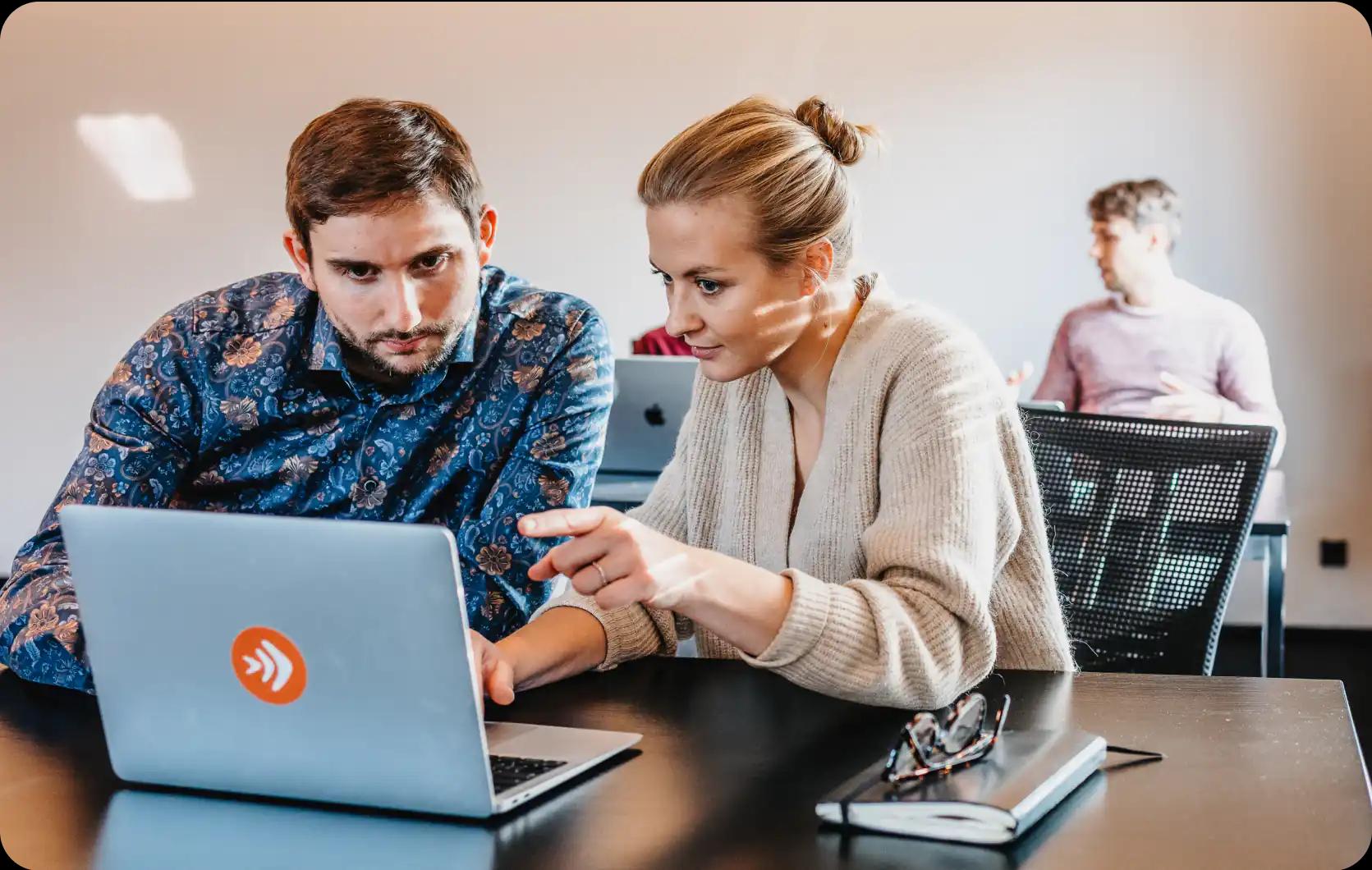 Zwei Personen arbeiten gemeinsam an einem Laptop in einem Büro.