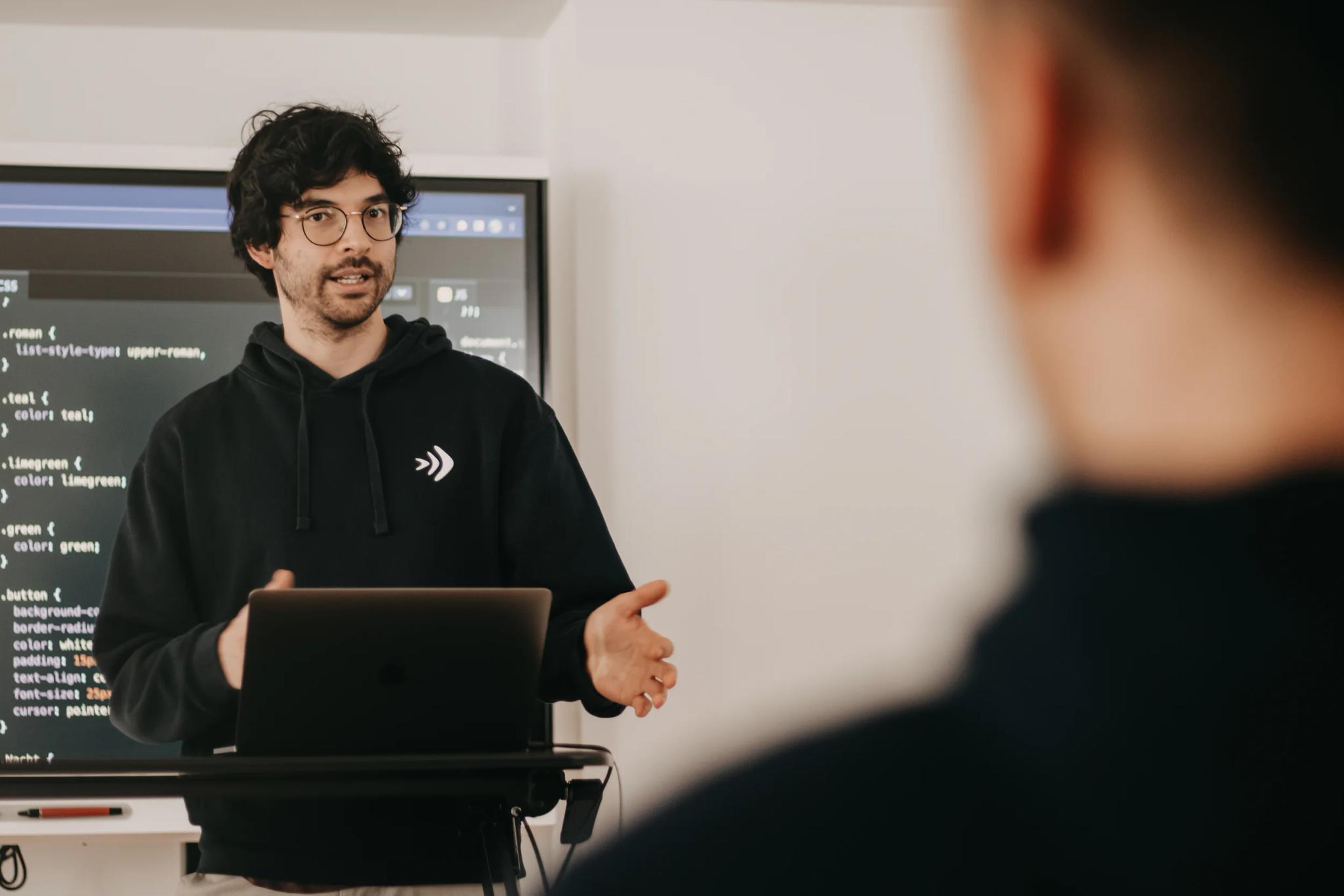 Mann gibt eine Präsentation vor einem Bildschirm mit Code